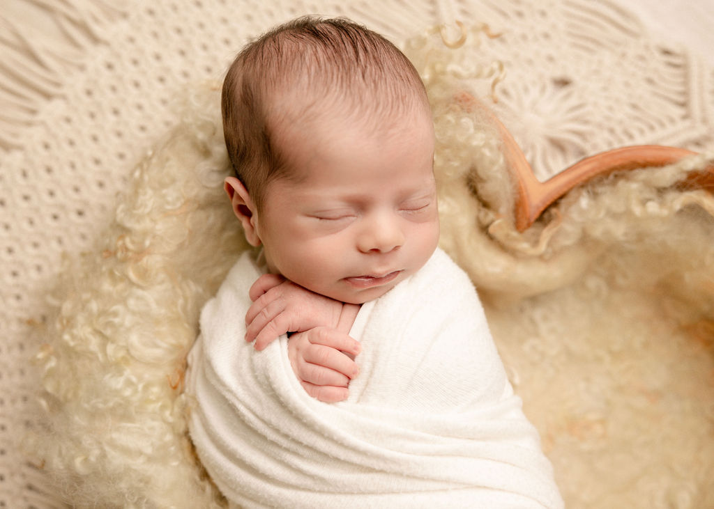 A newborn baby sleeps in a wooden bowl on blankets in a white swaddle after meeting long beach pediatric dentist