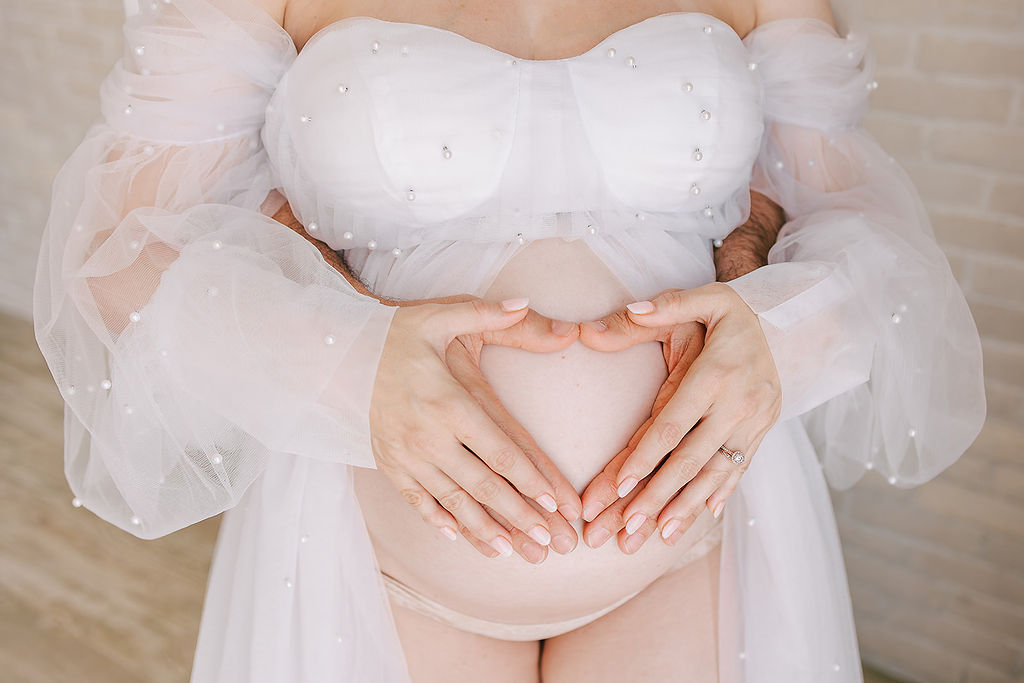 Details of a expecting parents holding their hands in a heart on the bump before meeting a Midwife in Long Beach