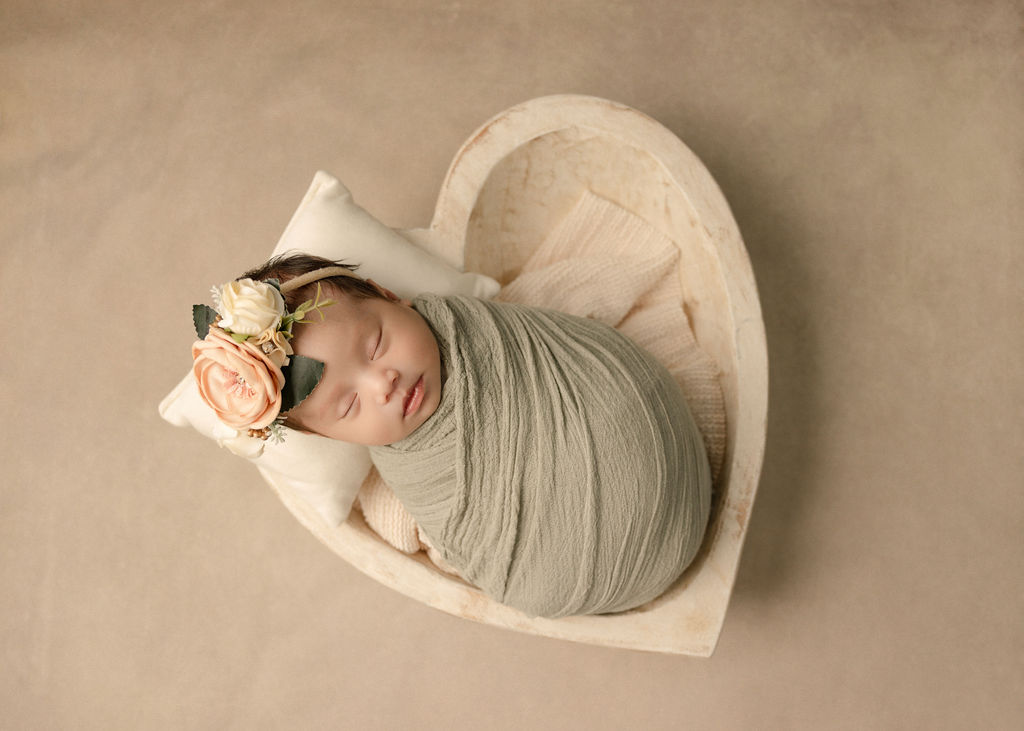 A newborn baby girl sleeps in a heart shaped bowl and green swaddle after meeting a nanny long beach