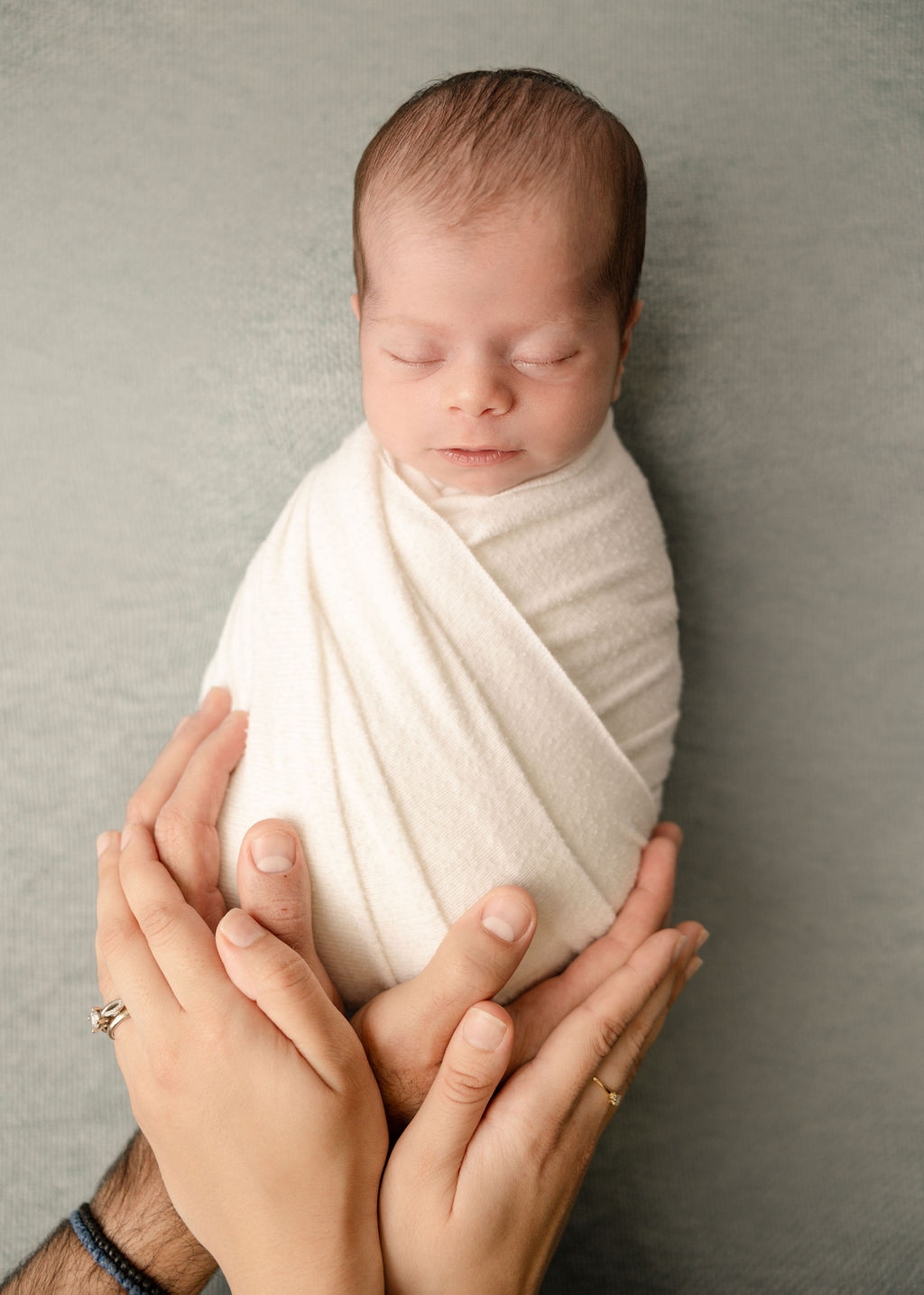 New parents rest their hands under their sleeping newborn baby in a tight white swaddle after some baby stores laguna beach