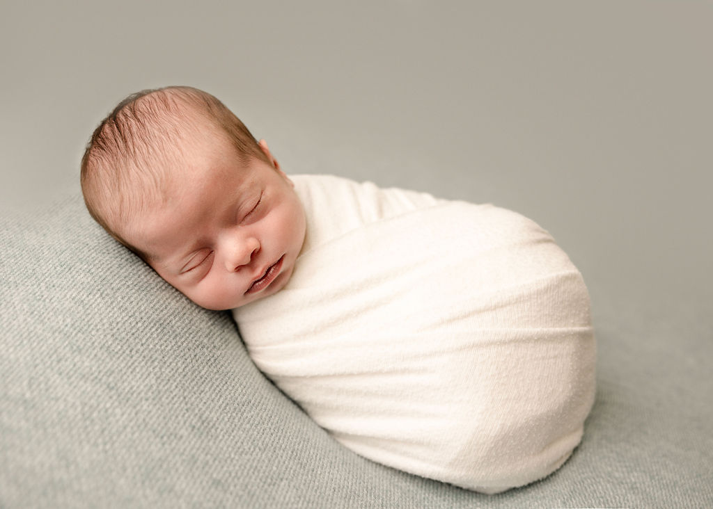 A newborn baby sleeps in a tight white swaddle in a studio ona pad after visiting baby stores laguna beach