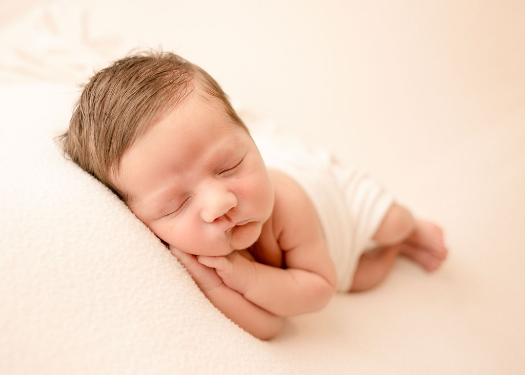 A newborn baby sleeps on its side on a white bed in a studio under a white blanket after using diaper service long beach