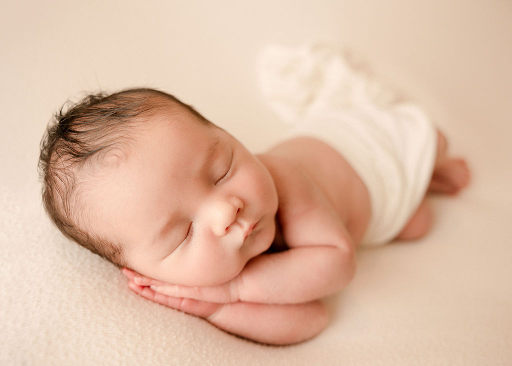 Close up of a newborn baby sleeping on a bed under a whtie blanket