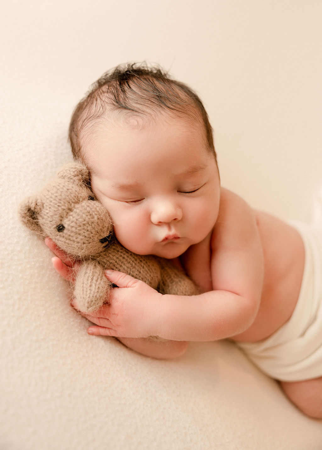 A newborn baby sleeps and cuddles on a knit teddy bear after some mommy and me classes long beach