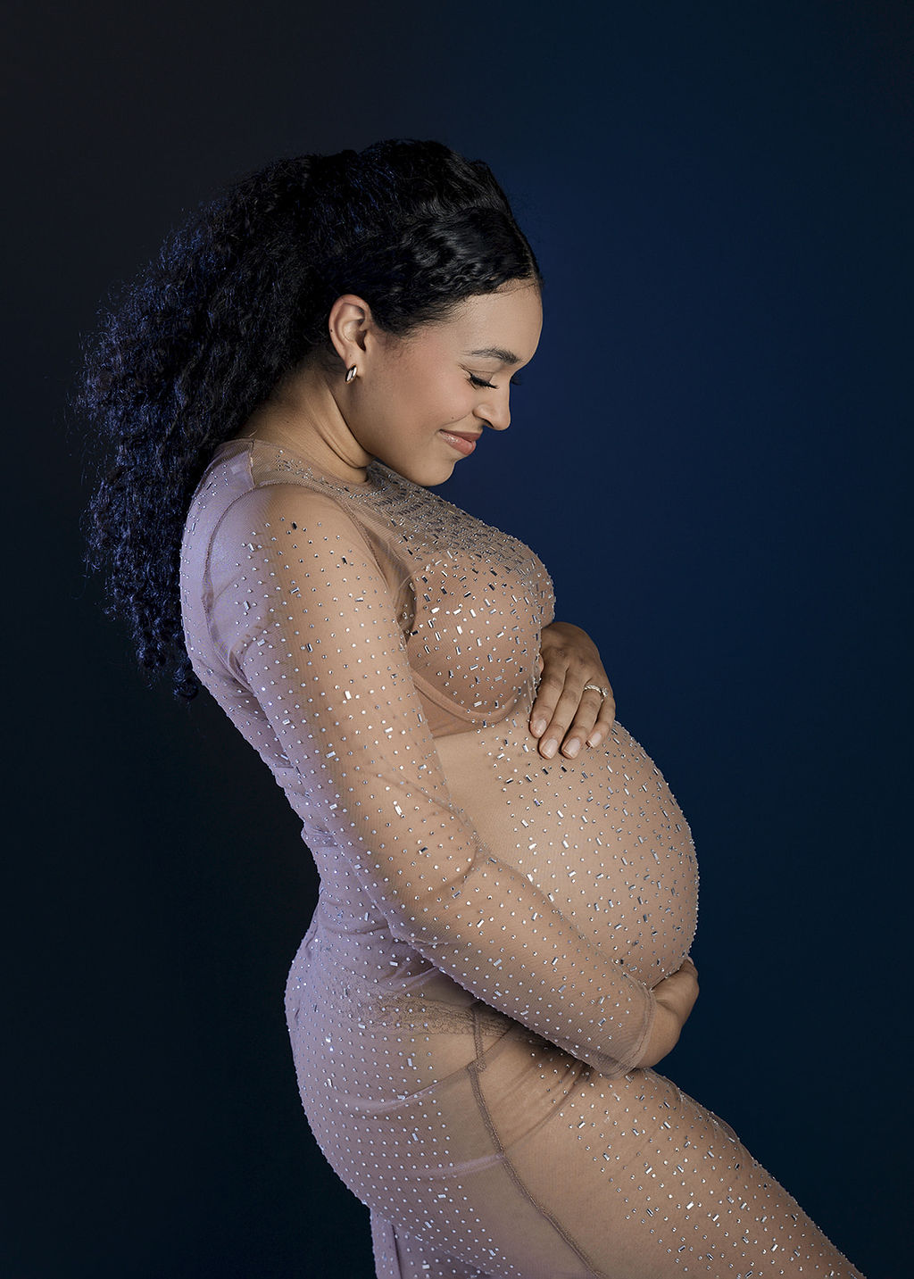 A mom to be in a nude color maternity gown smiling down at her bump in a studio after a prenatal massage long beach