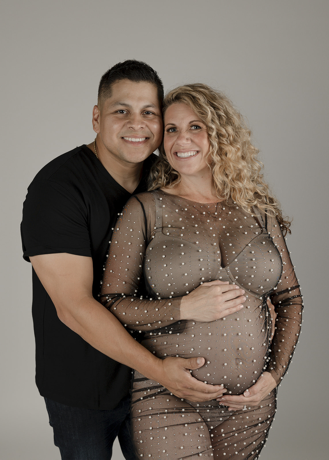 Happy expecting parents stand holding the bump in a studio touching cheeks after their 3D ultrasound in Boise