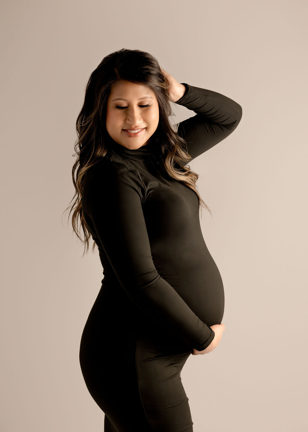 A smiling expecting mother stands with a hand in her hair in a studio in a black maternity gown after visiting a birth center in boise