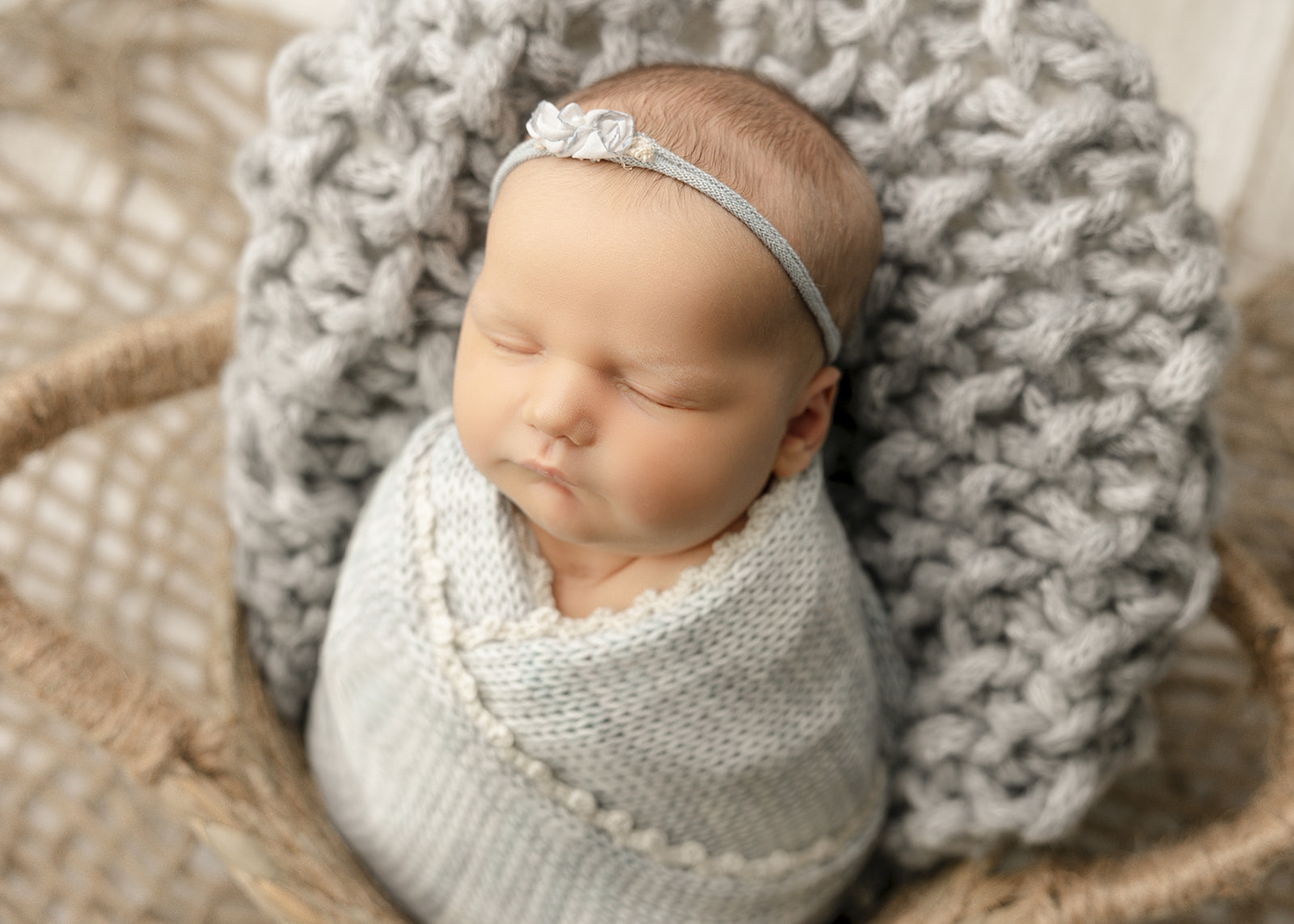 A newborn baby girl sleeps in a tight swaddle in a woven basket with a matching headband