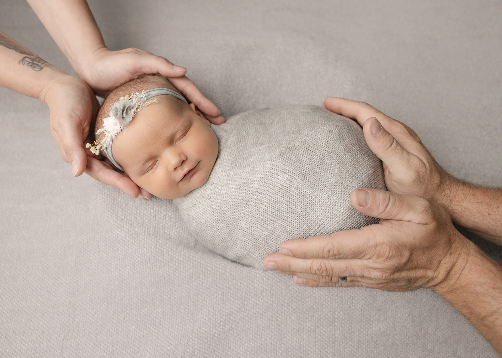 A newborn baby sleeps in mom and dad's hands in a grey swaddle after meeting a lactation consultant in Boise