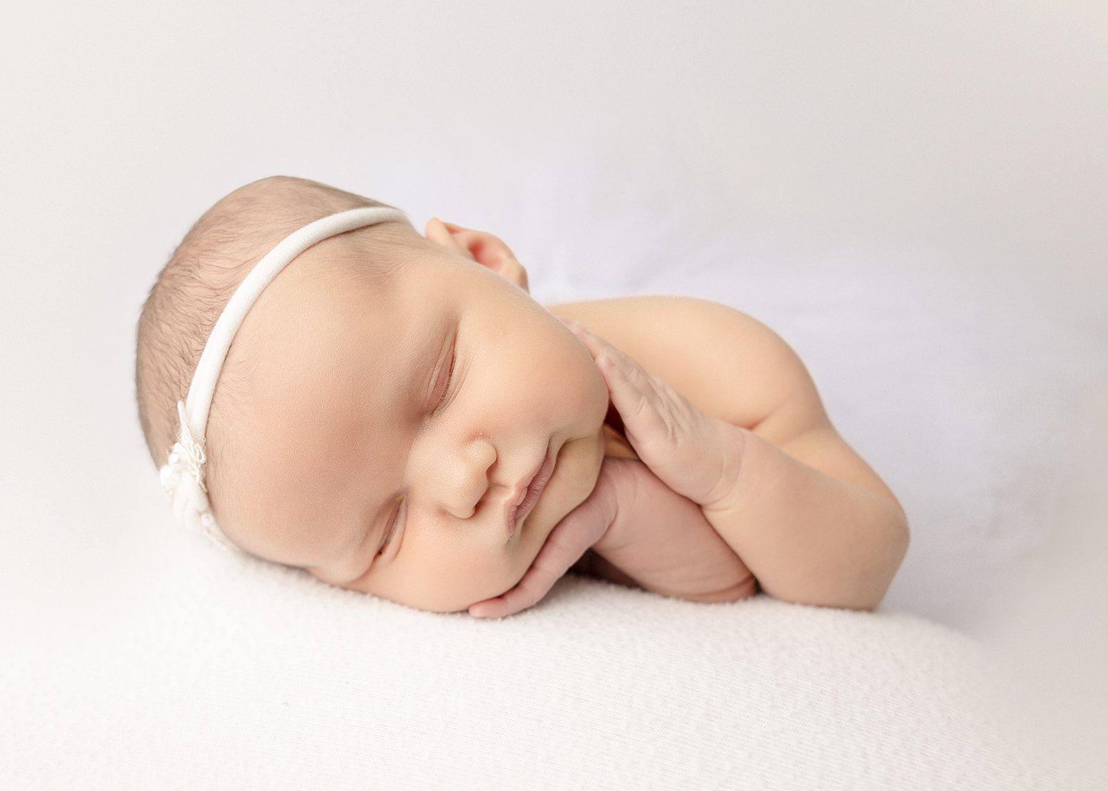 A newborn baby girl sleeps on her hand in a white headband in a studio after meeting a lactation consultant in Boise