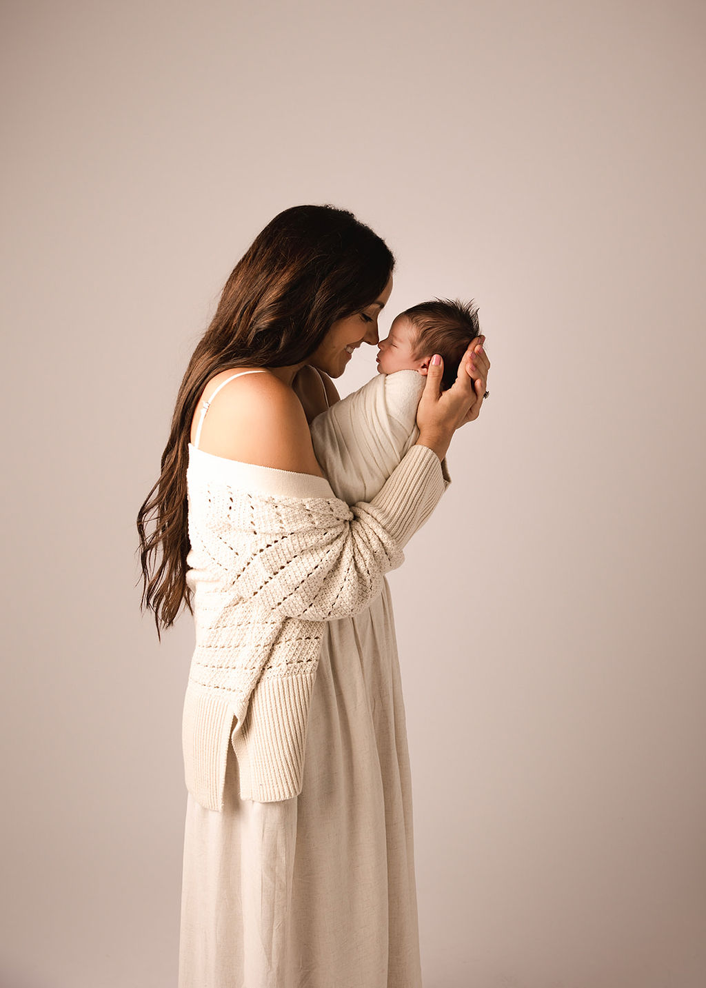 A happy new mother stands in a studio touching noses with her sleeping newborn baby after meeting a nanny in Boise