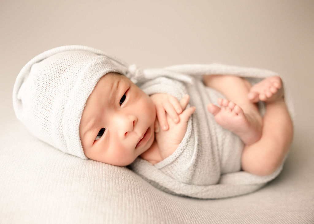 A newborn baby lays in an open swaddle with eyes open