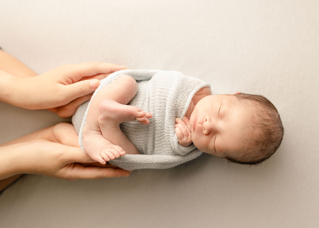 A mom and father hold their hands on their sleeping newborn baby before visiting a pediatric dentist boise