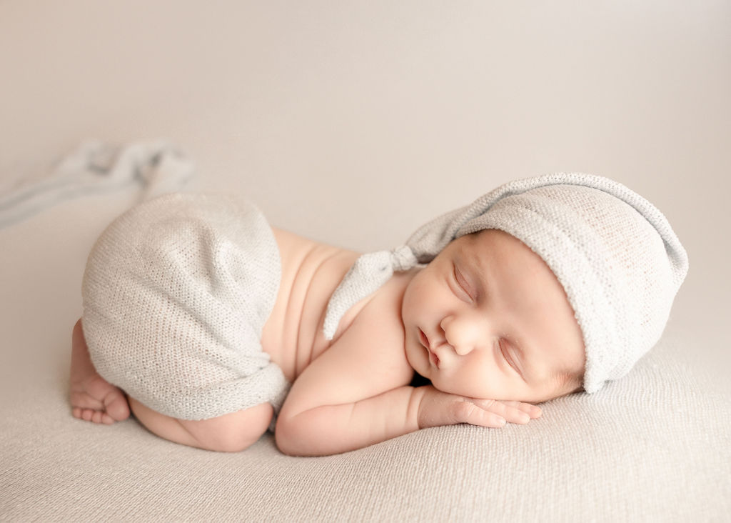 A newborn baby sleeps in a nightcap and loose blanket on its tummy before visiting pediatricians boise