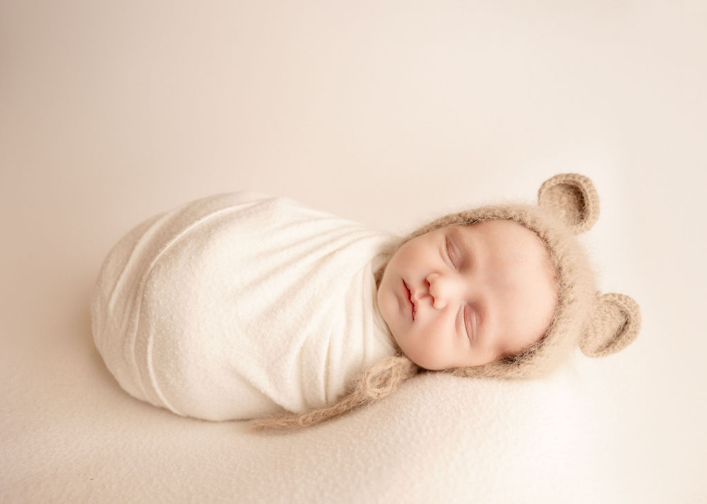 A newborn baby sleeps in a white swaddle and bear ears before visiting pediatricians boise