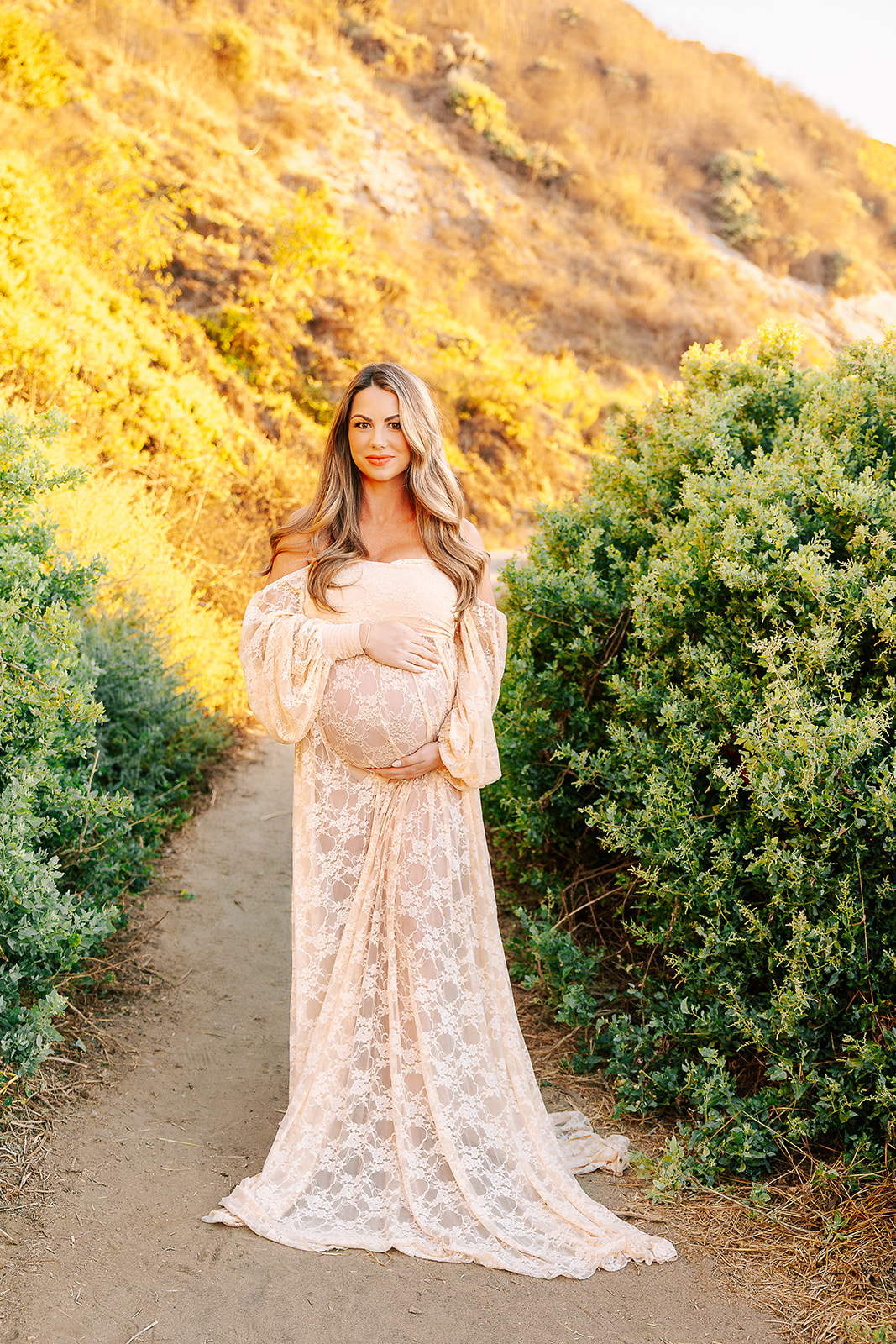 A happy mom to be in a cream lace maternity gown walks on a trail at sunset after some parenting classes in Boise