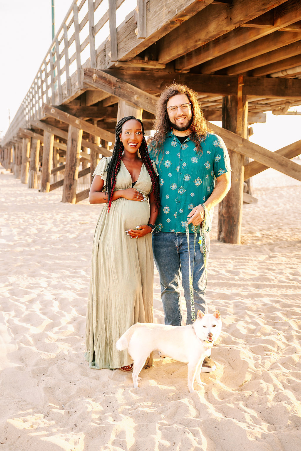 A happy expecting couple walks their dog while smiling on a beach at sunset after a prenatal massage in boise