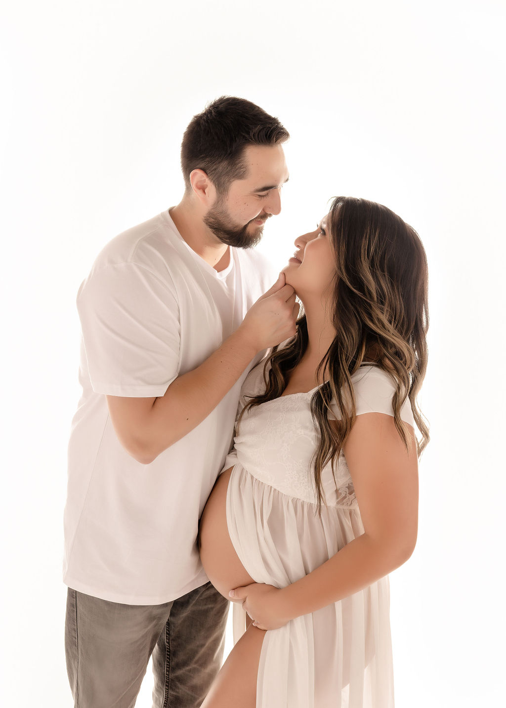 A happy expecting father snuggles his wife as they stand in a studio with the bump out