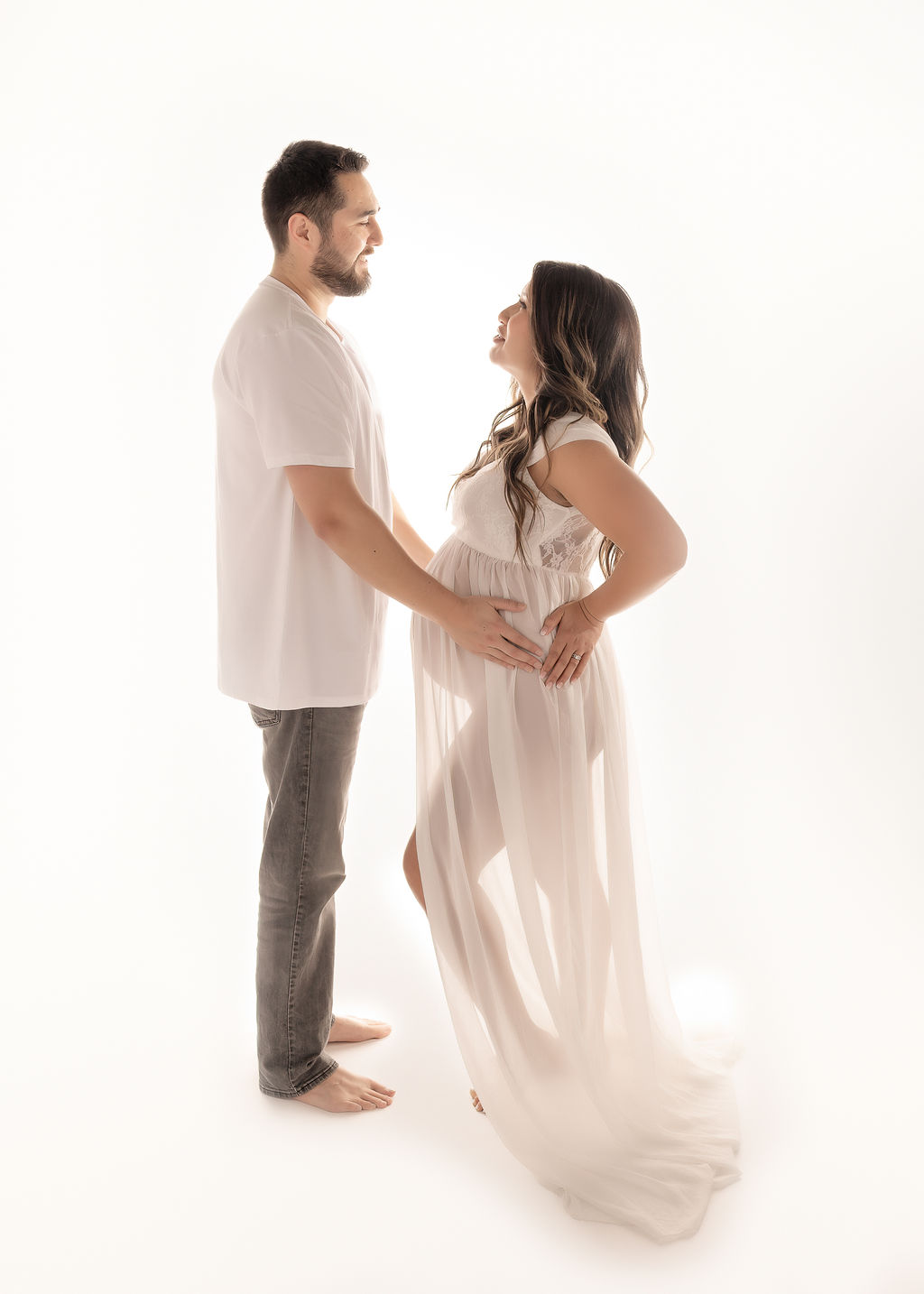 A happy expecting couple stands in a studio smiling at each other in white after some prenatal yoga in Boise